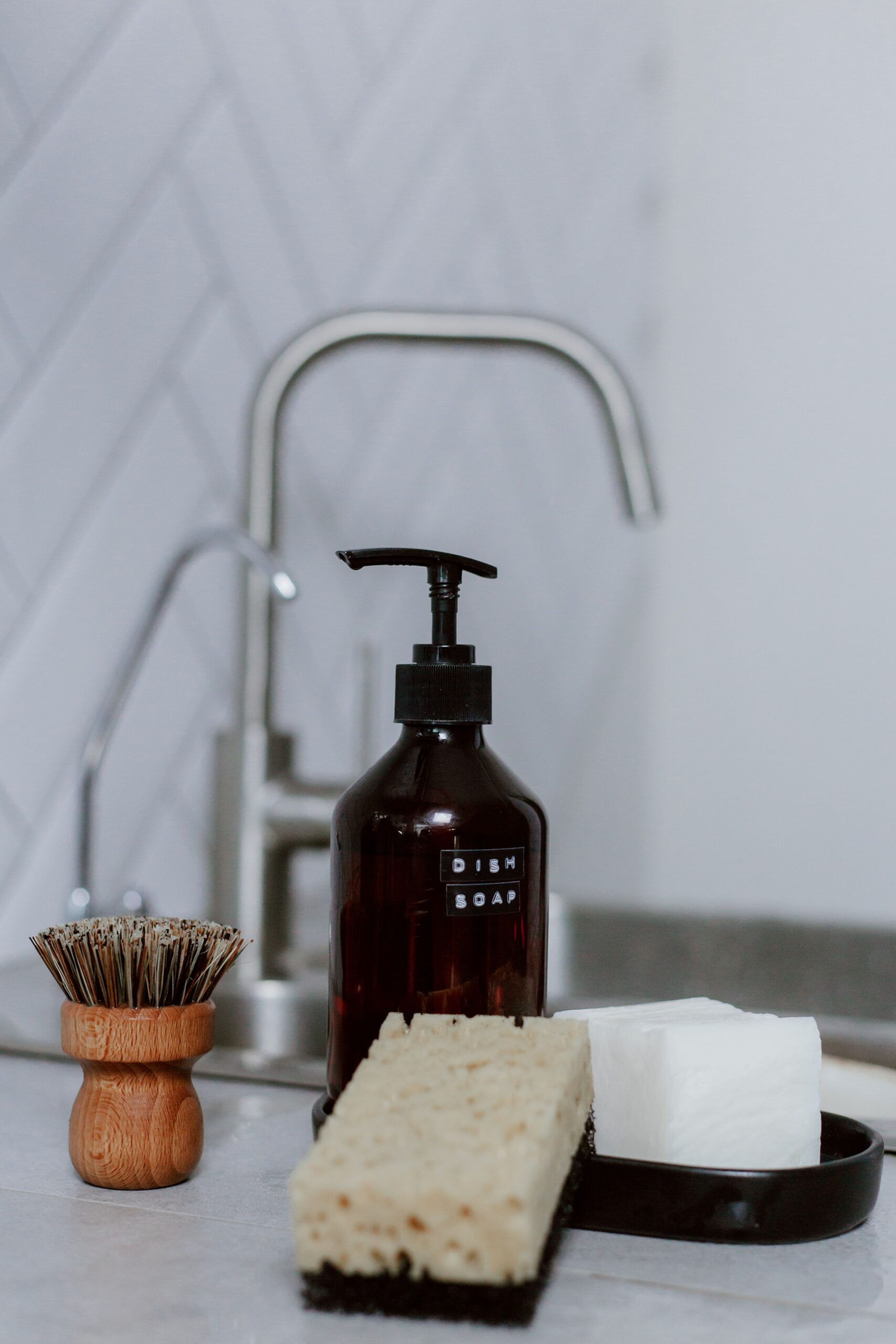 Dish soap, sponge and cleaning tools arranged beside a kitchen sink