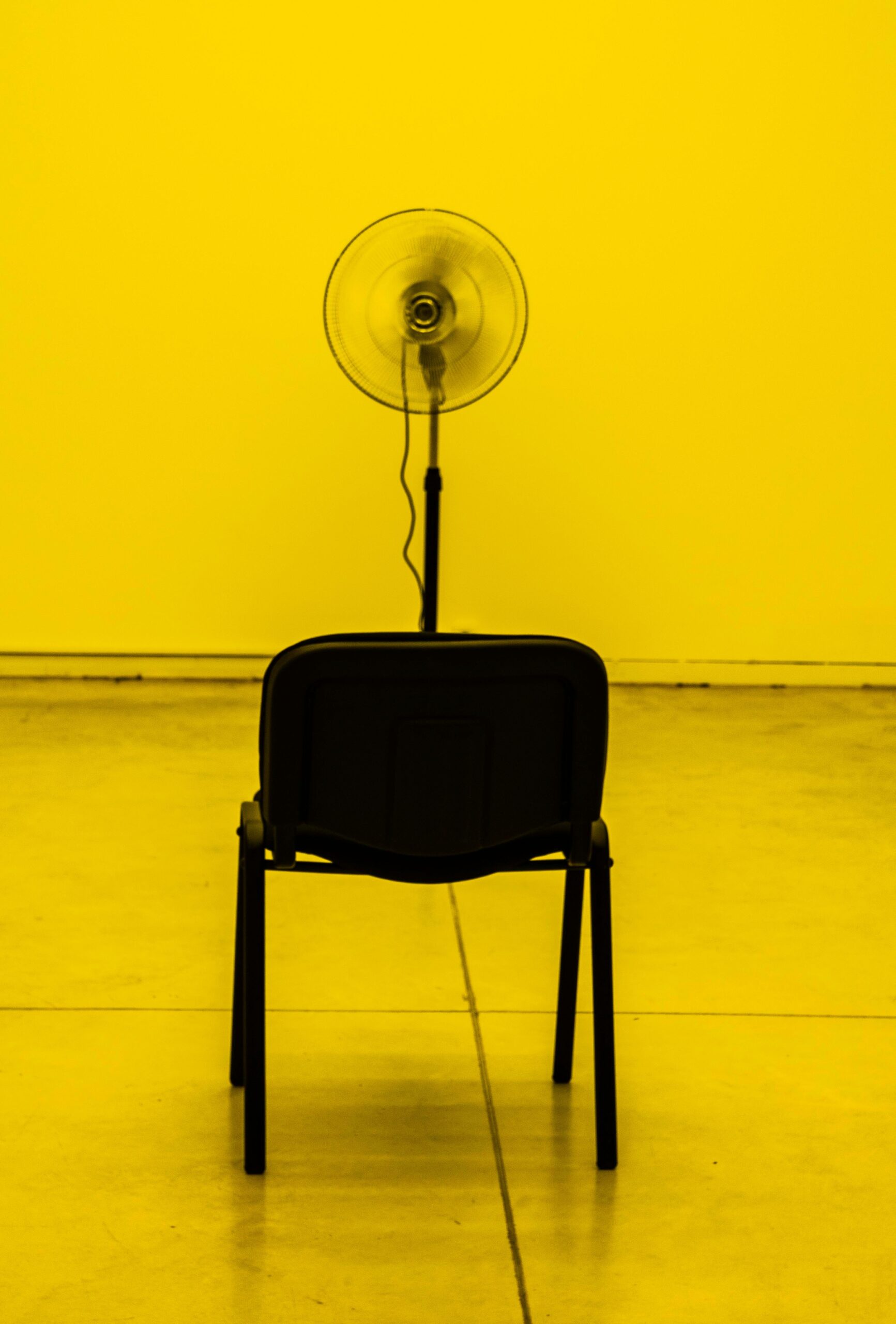 Black pedestal fan positioned behind a chair in an indoor room
