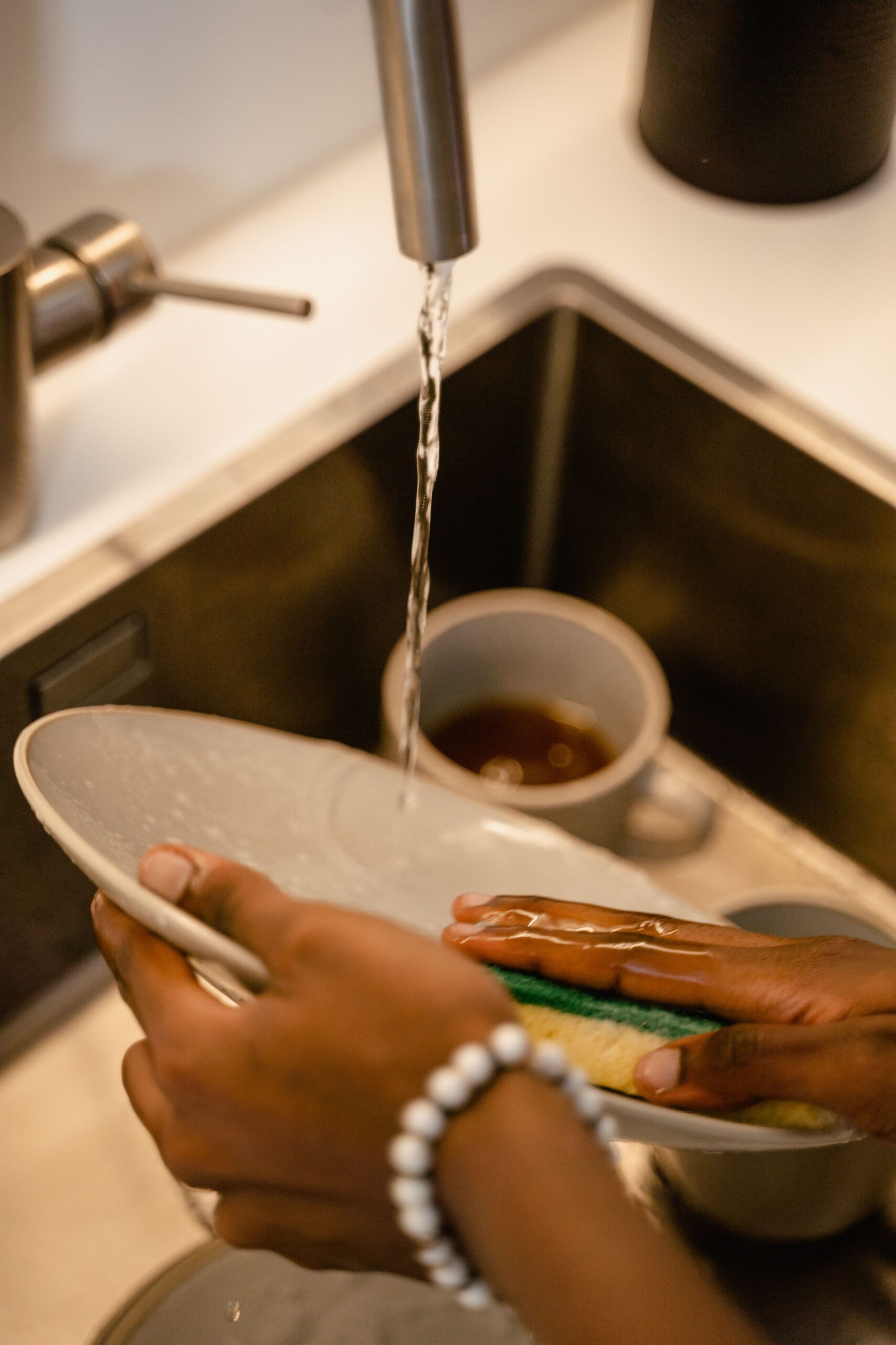 Person washing dishes with a sponge under a running kitchen faucet