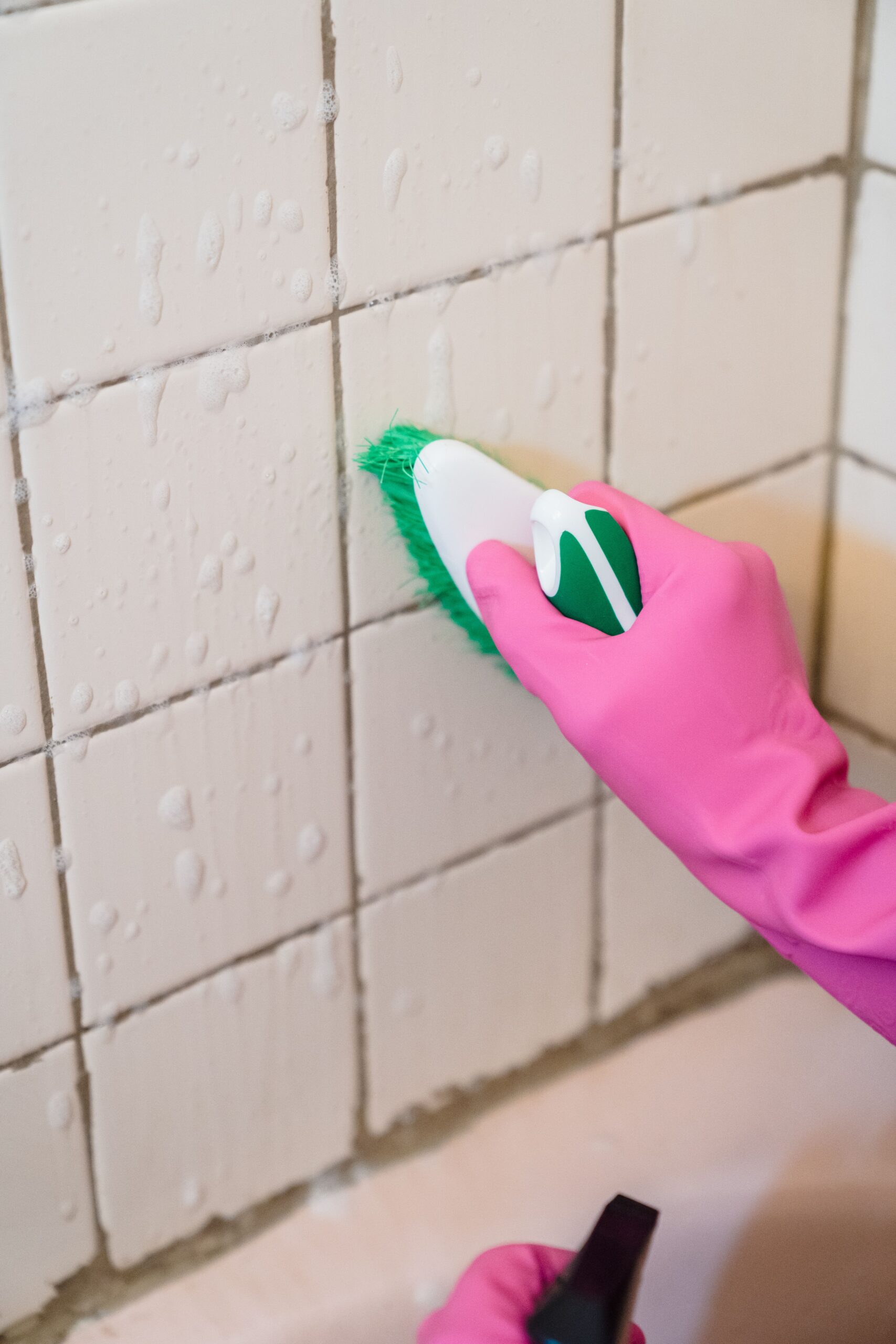 Gloved hand scrubbing bathroom wall tiles and grout